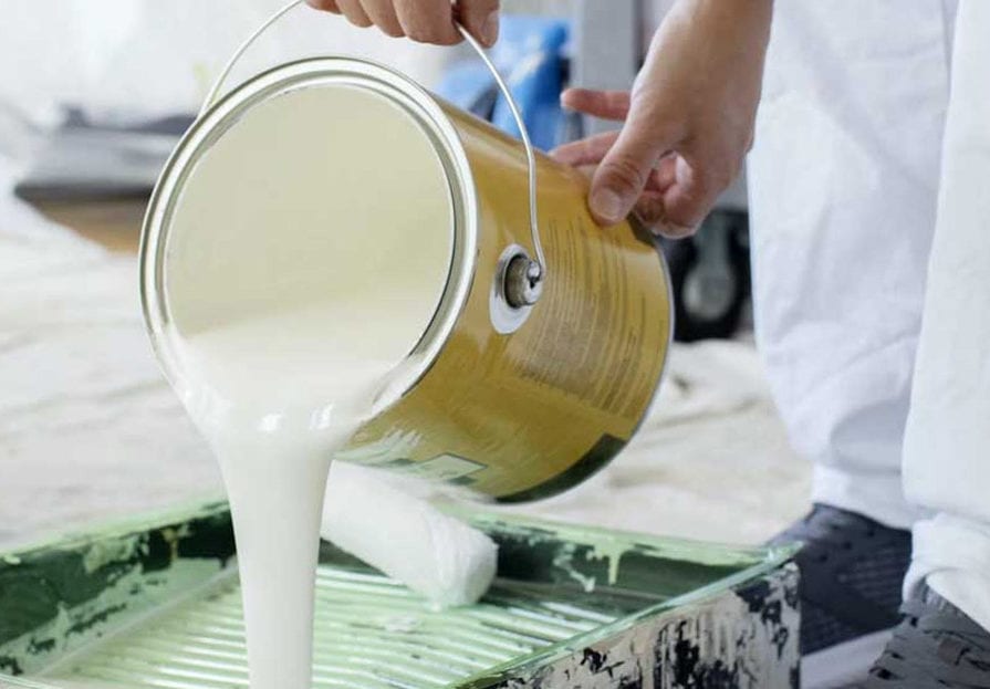 A can of white paint is poured into a paint rolling pan