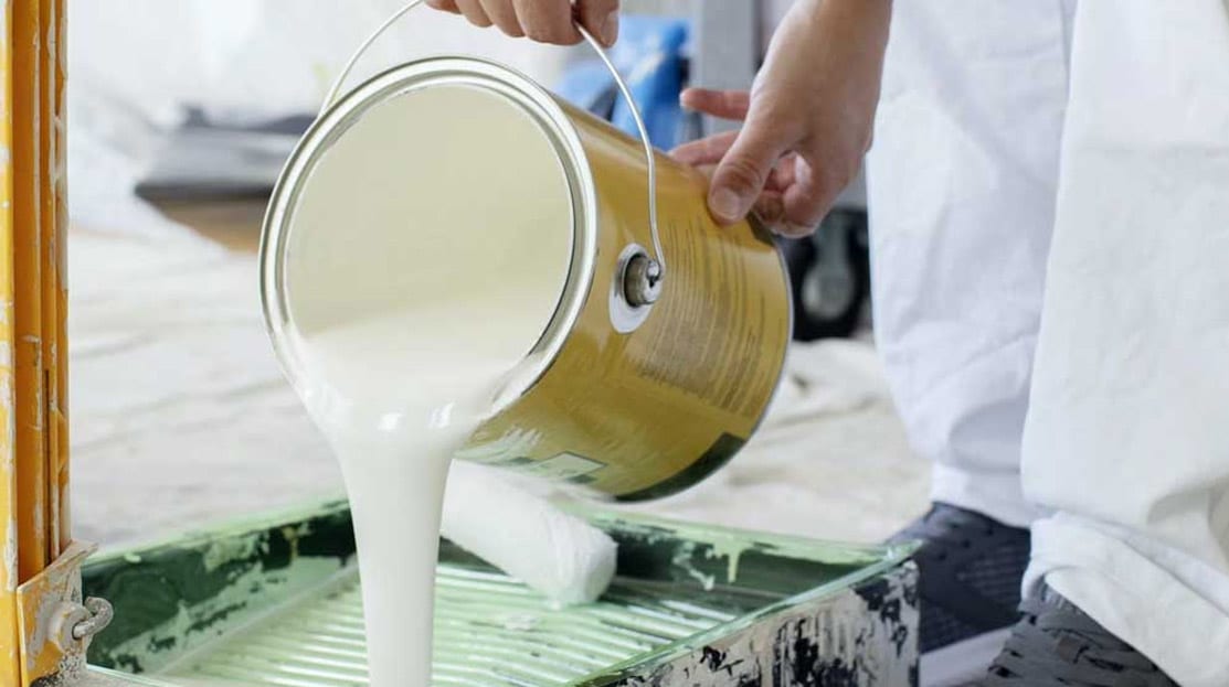 A can of white paint is poured into a paint rolling pan