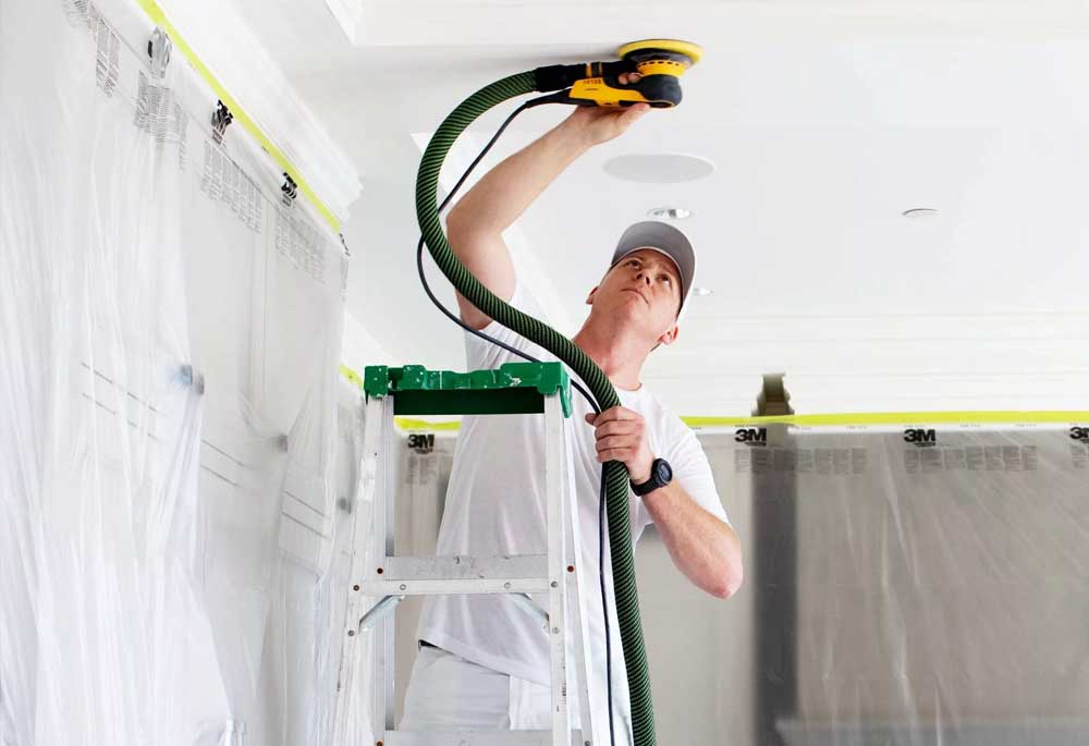 A Hemlock painter uses a dustless sanding machine to prepare surfaces for interior painting.