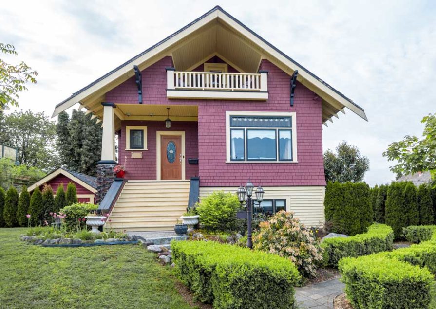 A red house that has been expertly painted, with light wood accents, by Hemlock Painting.