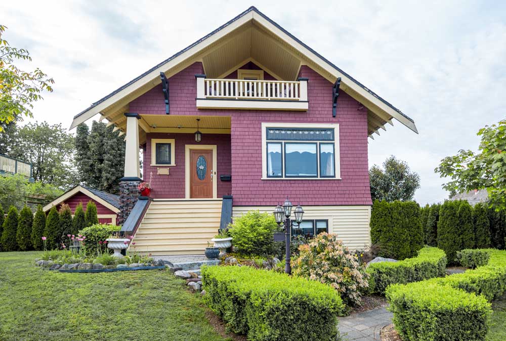 A red house that has been expertly painted, with light wood accents, by Hemlock Painting.