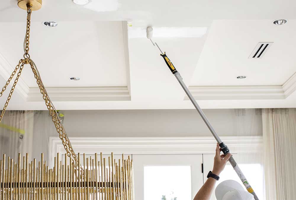 A Hemlock Painting employee expertly paints a ceiling white; we are proud to provide the best in interior house painting services.