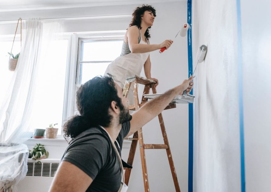 A man and a woman apply paint to a wall with paint rollers
