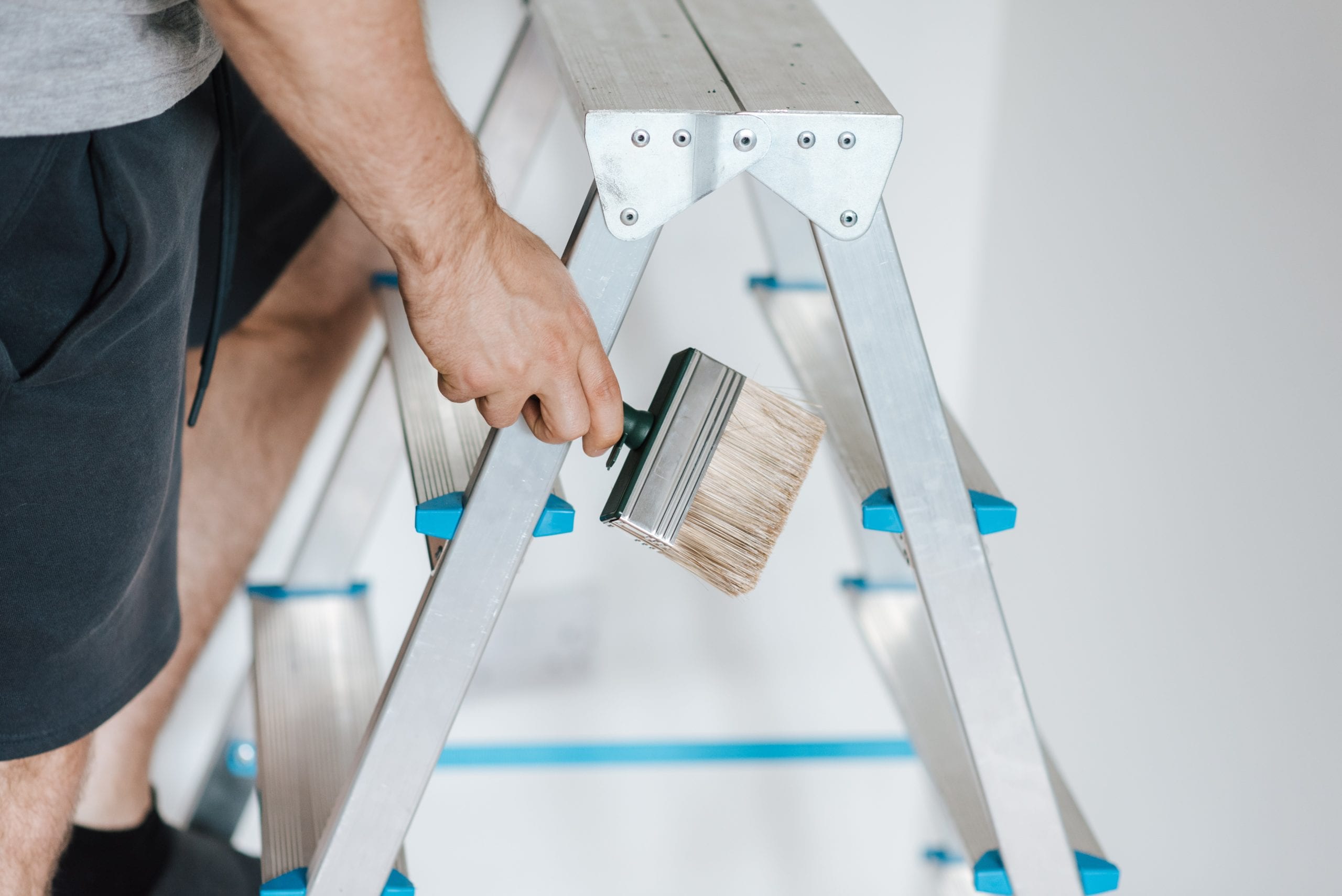 A man stands on top of a ladder holding a large paintbrush