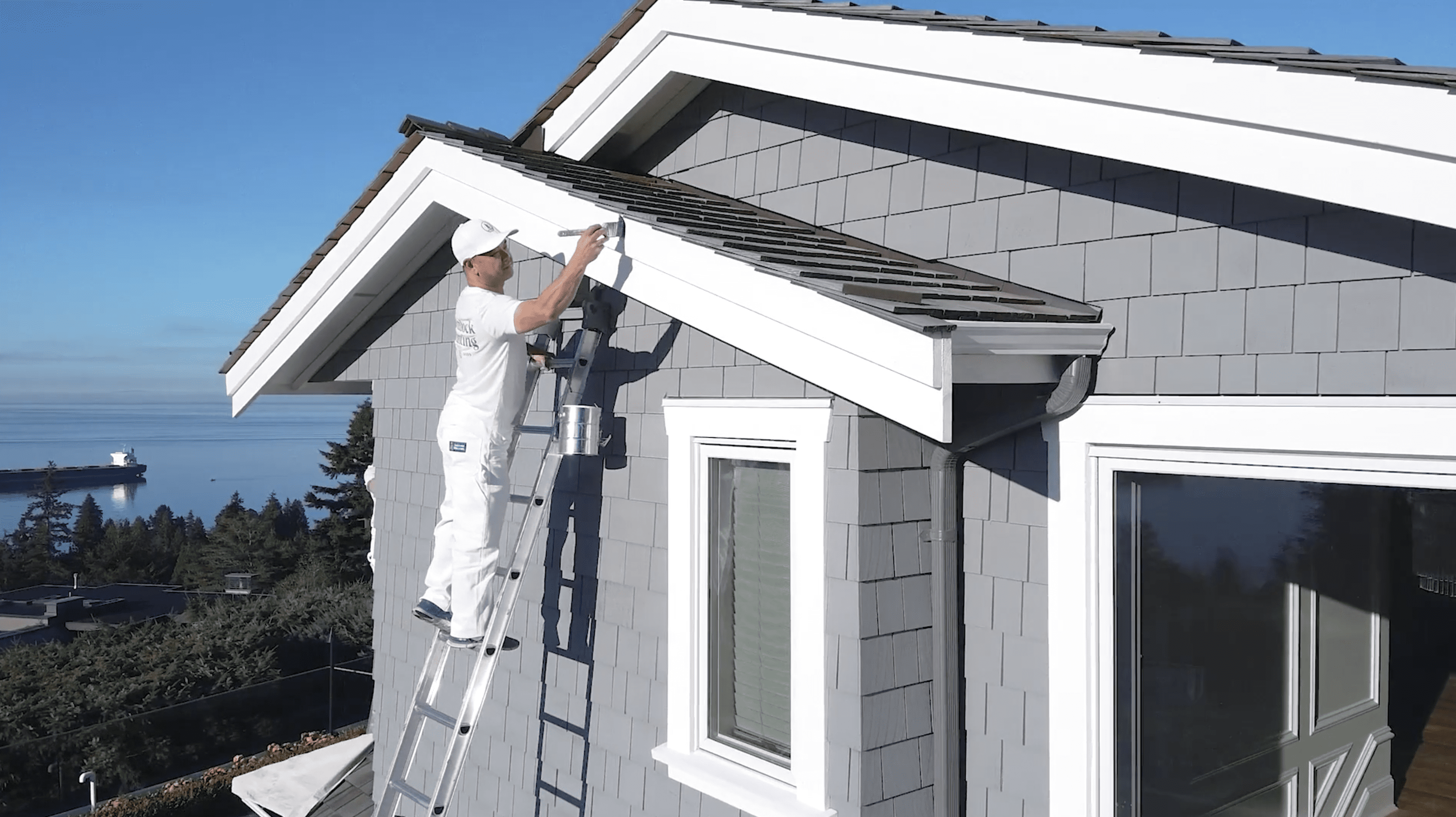 A Hemlock Painting crew member paints an exterior area below the roof of a house.